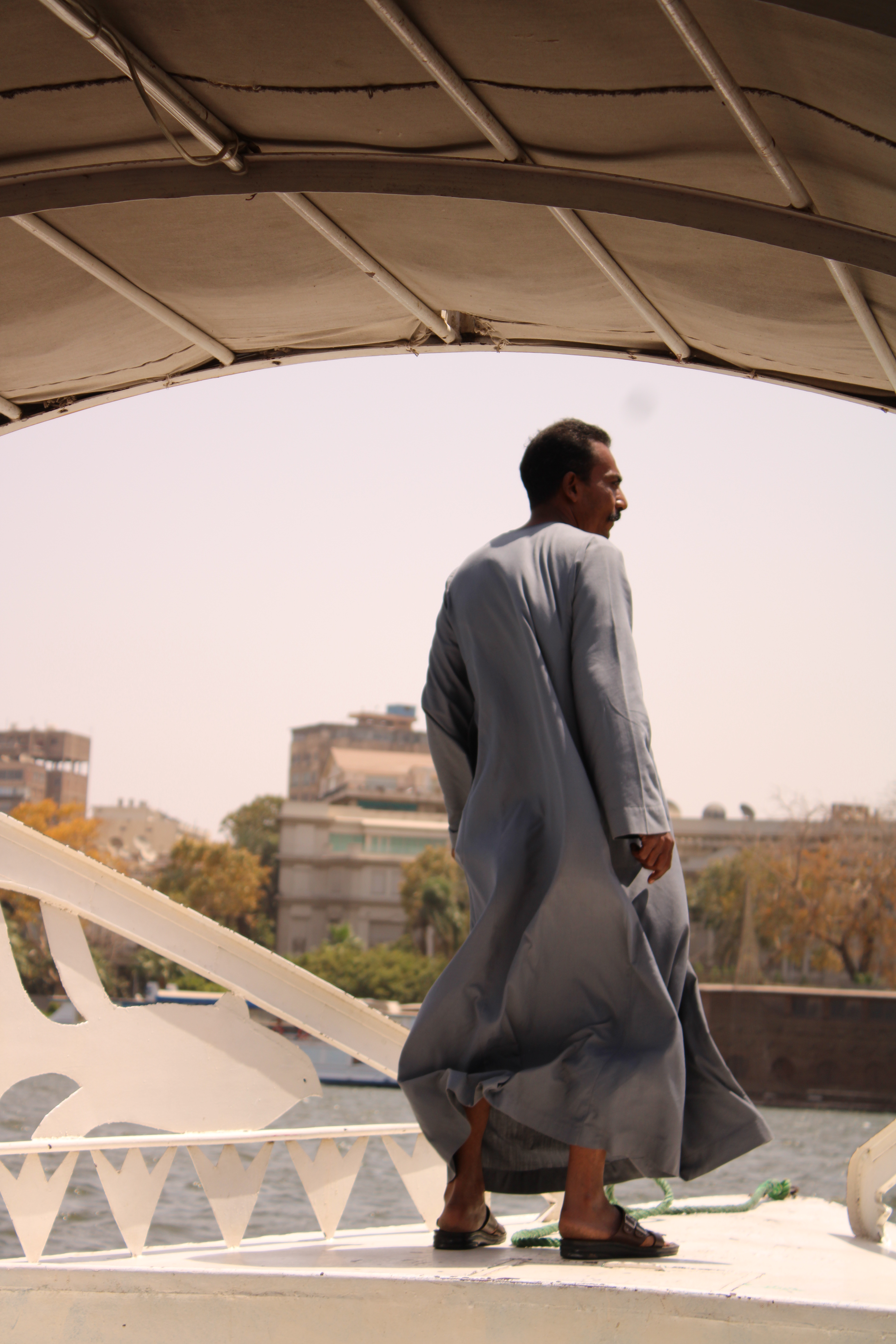 Croisière sur le Nil : Homme égyptien en djellaba bleu-gris, sur le pont du bateau.